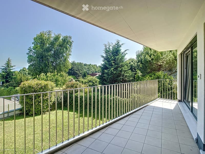 Balcony with tiled floor, metal railing, and view of green trees and a clear blue sky.