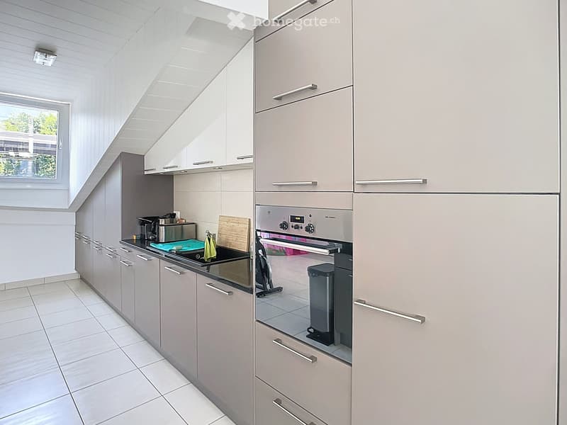 Modern kitchen with light grey cabinets, stainless steel oven, coffee maker, and cutting board on the counter.