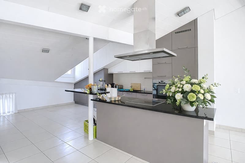 Modern kitchen with white cabinets, stainless steel appliances, and a central island. Features include a range hood, refrigerator, oven, stove, and a vase with flowers on the island.