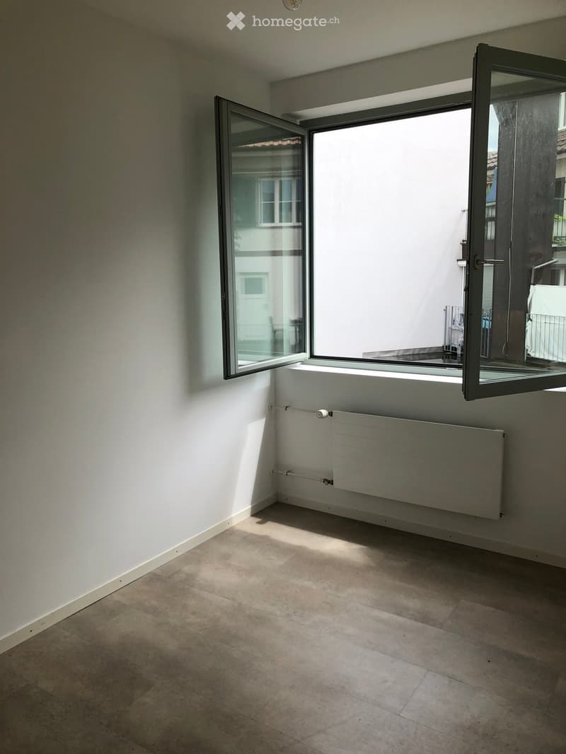 Empty room with tiled floor, white walls, and large open window with a radiator below.
