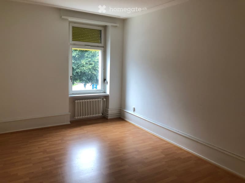 Empty room with wooden flooring, white walls, and a window with blinds. A radiator is visible below the window.