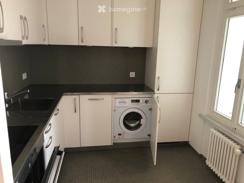 Compact kitchen with white cabinets, black countertops, a sink, and a built-in washing machine.