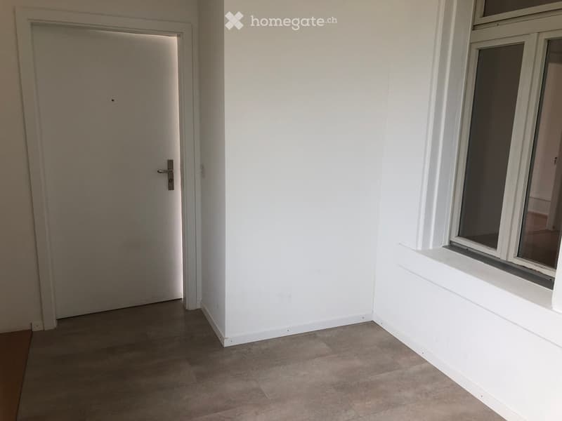 Empty room with white walls, tiled floor, and a single door leading to another space. A window with white frame is visible on the right side.