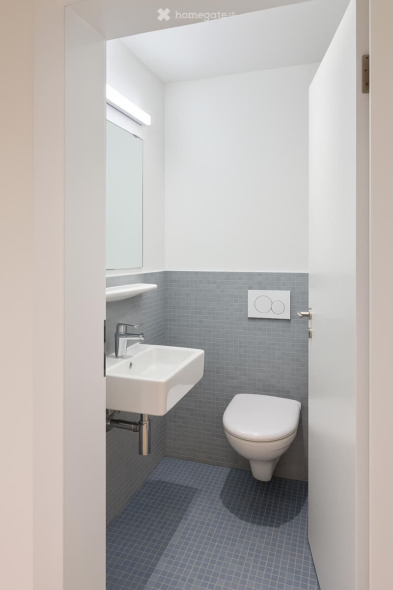 Modern bathroom with white walls, blue tiled lower half, white sink, chrome faucet, toilet, and a small mirror above the sink.