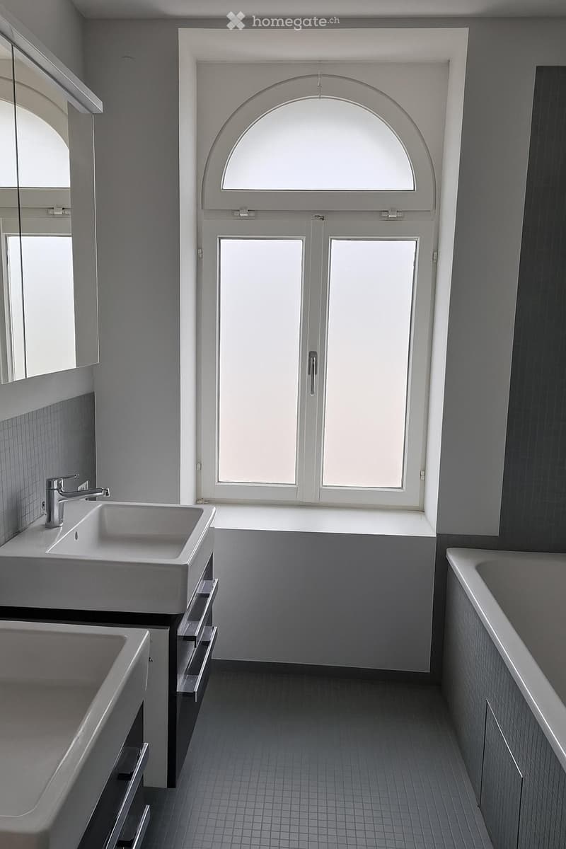 Modern bathroom with a double sink, bathtub, large window, and mirrored cabinet.