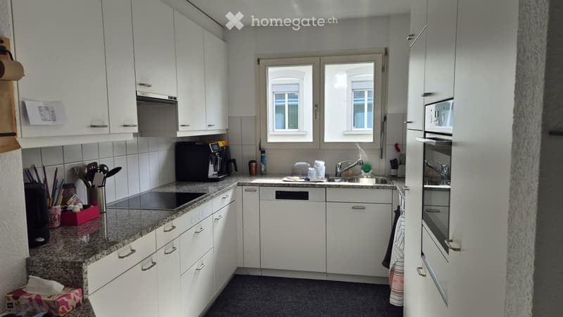 Modern kitchen with white cabinets, granite countertop, built-in oven, dishwasher, and various appliances.