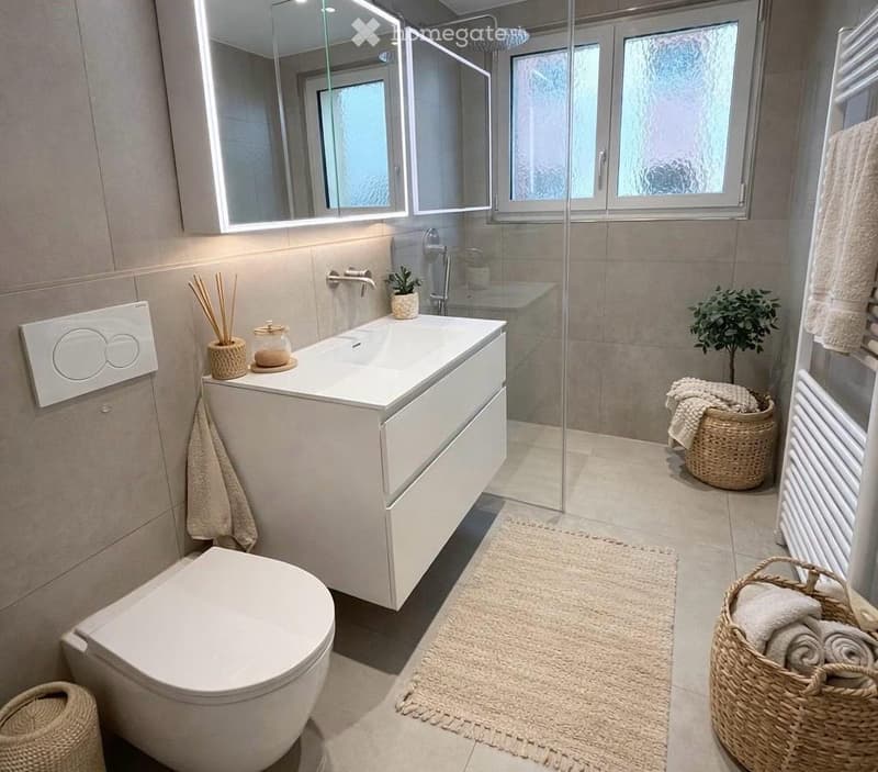 Modern bathroom with a white sink, toilet, large mirror, glass shower enclosure, wicker baskets, and a small plant.