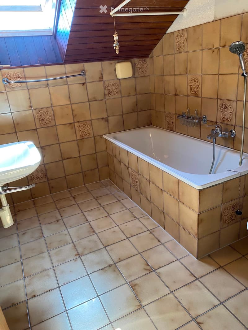 Bathroom with beige tiles, a bathtub, a sink, a showerhead, and a towel rack. The walls feature decorative floral tiles.