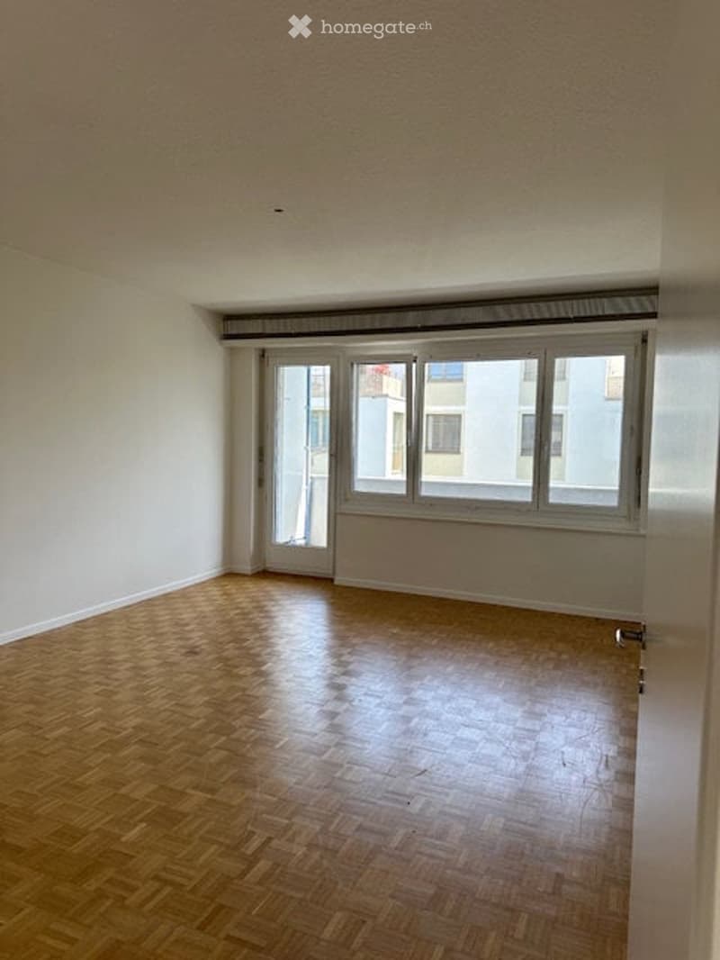Completely empty room with wooden flooring, large windows, and a sliding glass door leading to a balcony.
