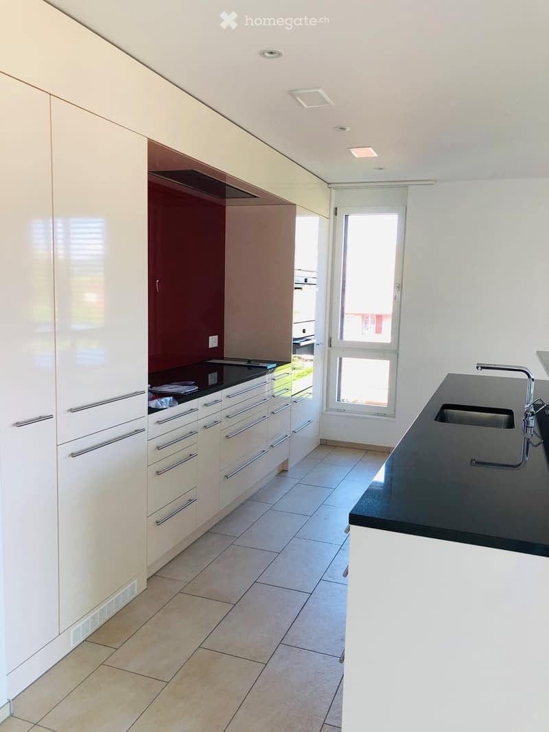 Modern kitchen with white cabinets, black countertop, and stainless steel sink. Features a window with blinds and a door leading outside.