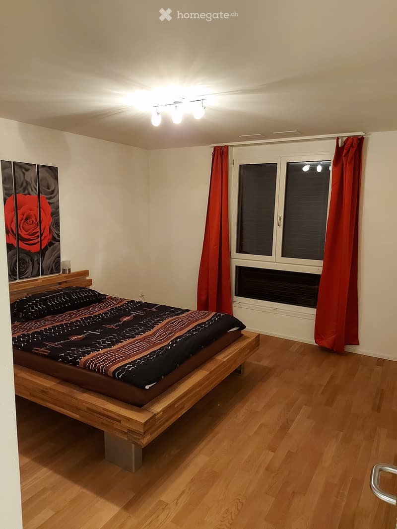 Modern bedroom with wooden flooring, a raised platform bed, red curtains, and a decorative picture frame on the wall.