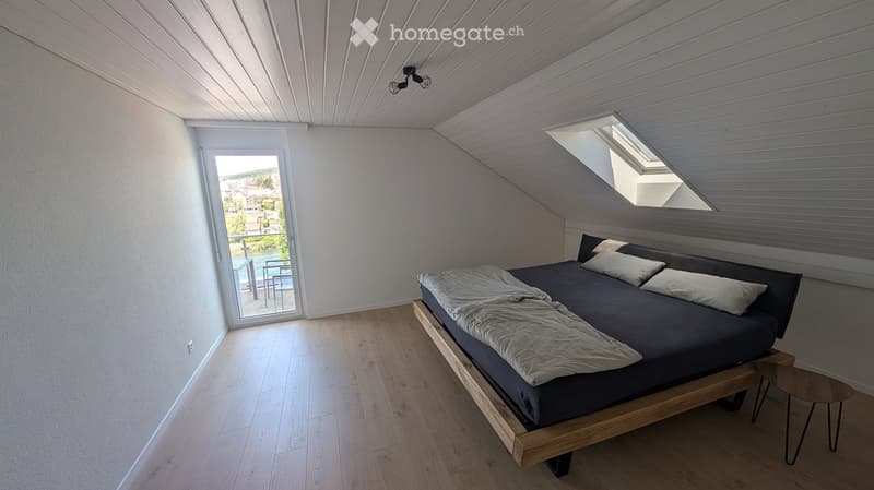 Modern bedroom with wooden floor, slanted ceiling, skylight windows, and a view of the outdoor area.