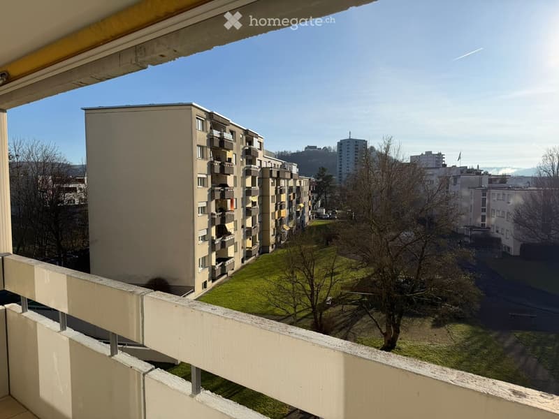 Balcony overlooking a residential area with apartment buildings, green spaces, and distant cityscape.