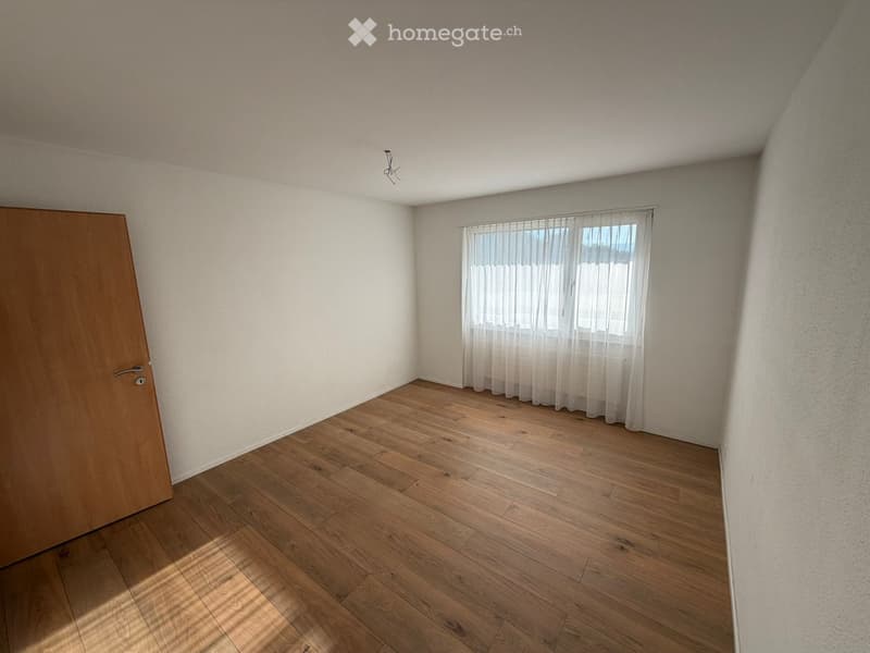Empty room with wooden flooring, white walls, and a window with sheer curtains. No furniture or equipment present.