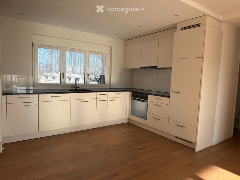 Modern kitchen with white cabinets, wooden flooring, and a large window overlooking a snowy landscape.