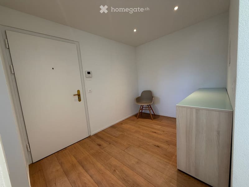 A small, unfurnished room with wooden flooring, a single chair, and a small table.