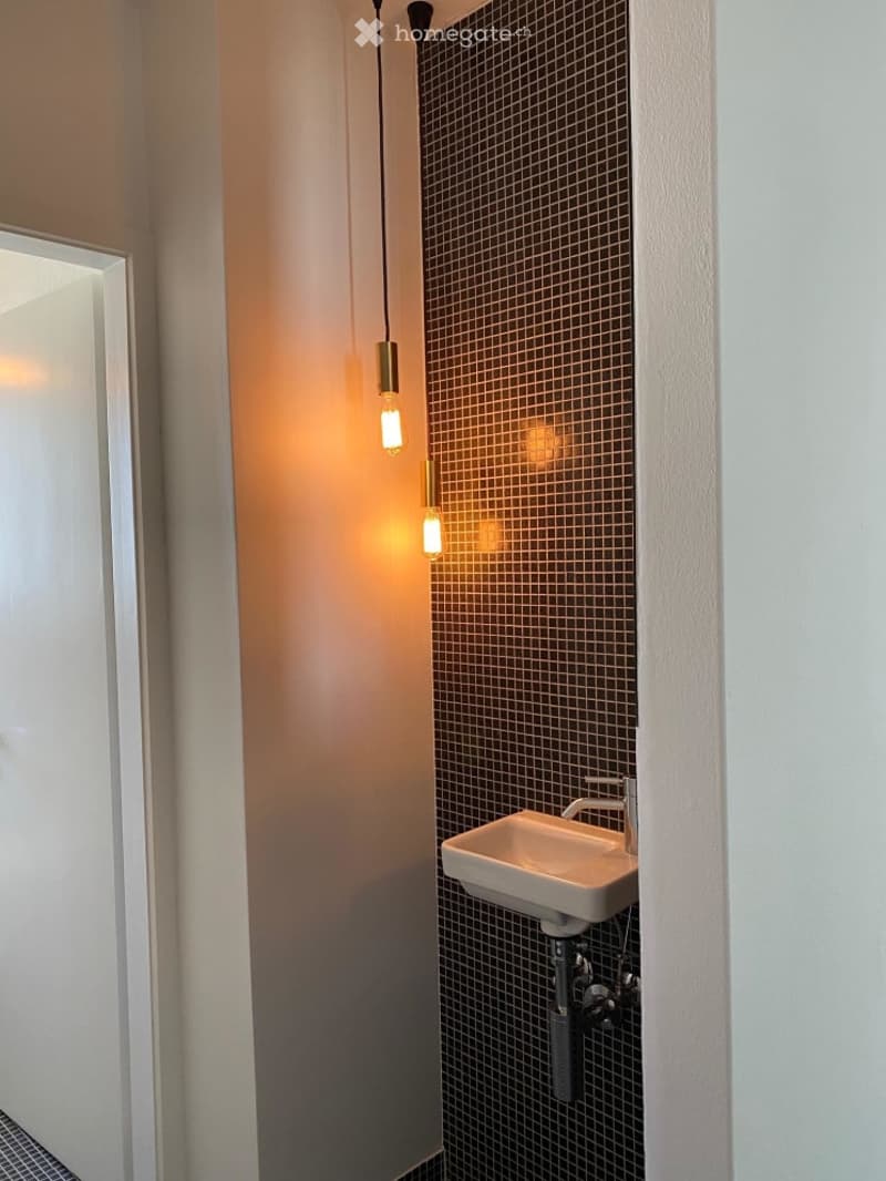 small bathroom with white sink, black tiled wall, three hanging lamps
