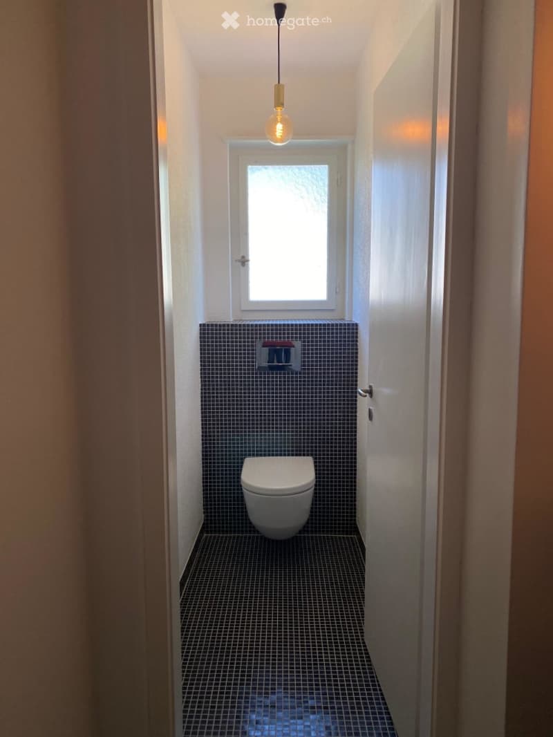 small bathroom with toilet, window, tiled floor, white walls, hanging light
