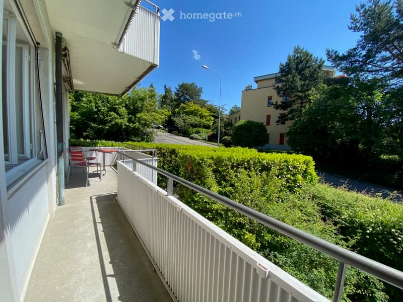 Balcony with metal railing, table and chairs, view of trees and street