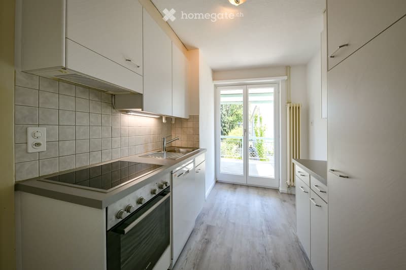 Modern kitchen with white cabinets, stainless steel oven, sink, and faucet. Light wooden flooring and a sliding glass door leading to an outdoor area.