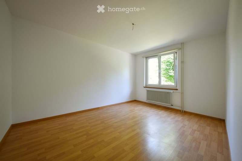 Empty room with wooden flooring, white walls, and a single window with a radiator below it.