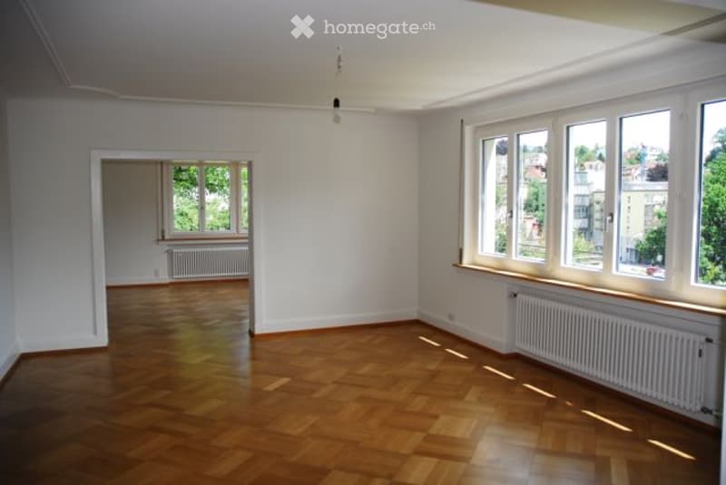 Empty room with wooden flooring, white walls, and large windows allowing natural light. No furniture or equipment present.