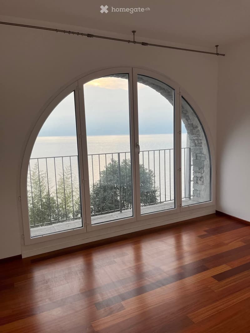 large arched window, balcony with metal railing, wooden flooring, view of the ocean