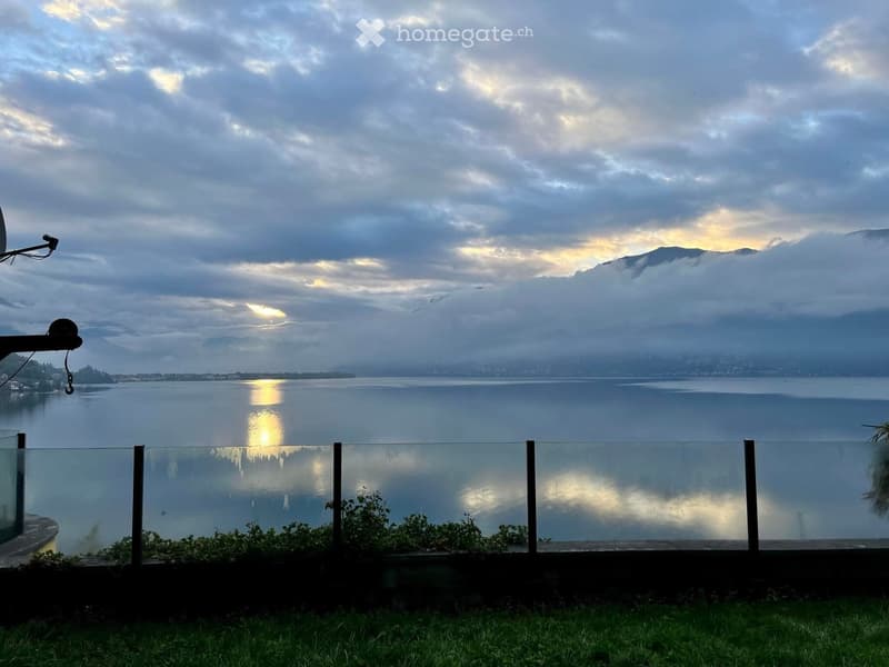 A view of a lake with mountains in the background, a cloudy sky, and a fence.