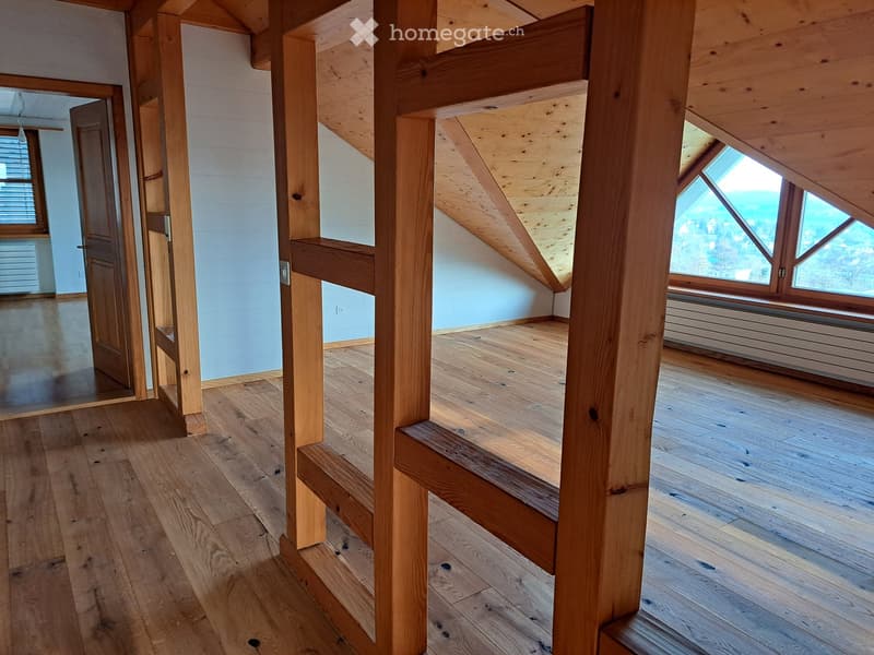 Empty attic space with wooden beams, wooden floor, and skylight windows offering a view of the outdoors.