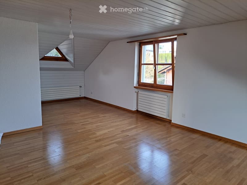 Empty room with wooden flooring, white walls, and large windows allowing natural light. The ceiling has exposed wooden beams and a skylight. There is a radiator under one window and a light fixture hanging from the ceiling.