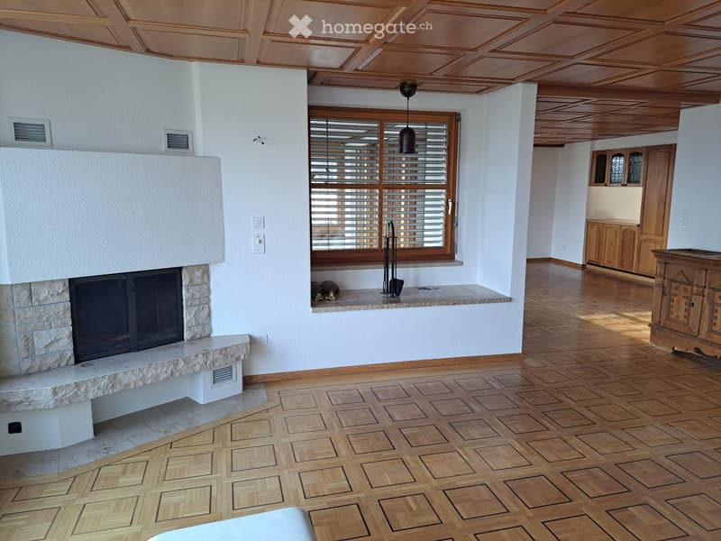 Spacious living room with wooden parquet flooring, a stone fireplace, a large window with blinds, and a wooden cabinet.