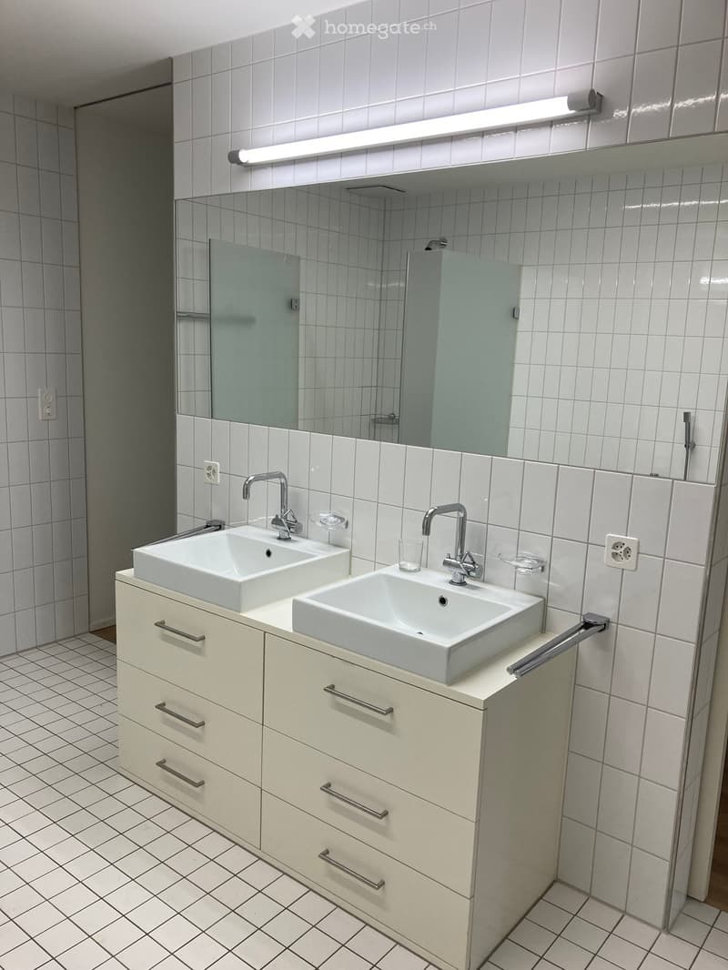 Modern bathroom with two white sinks, chrome faucets, a large mirror, and a cream-colored cabinet with multiple drawers.