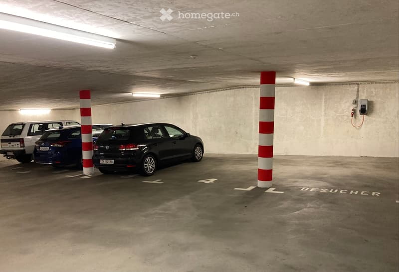 Underground parking area with several parked cars, concrete pillars, and marked parking spaces.