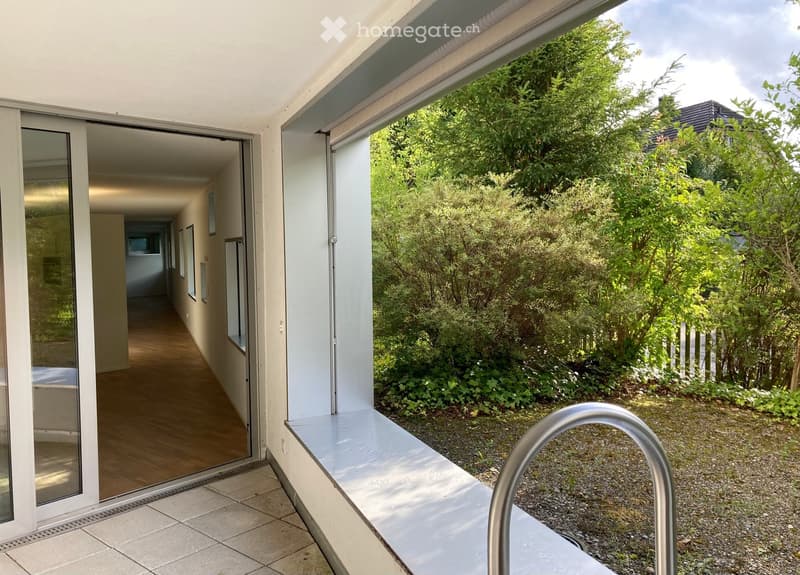 Modern hallway with wooden flooring, white walls, large glass sliding doors leading to a lush green garden area.