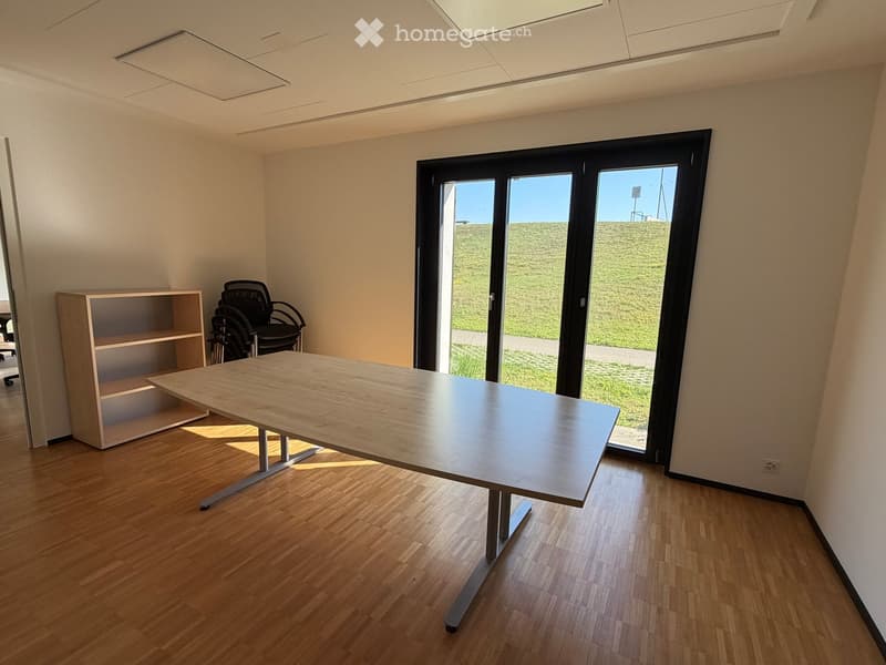 Bright, unfurnished room with wooden flooring, large sliding glass door leading to outdoor area, a table, a chair, and a shelf.