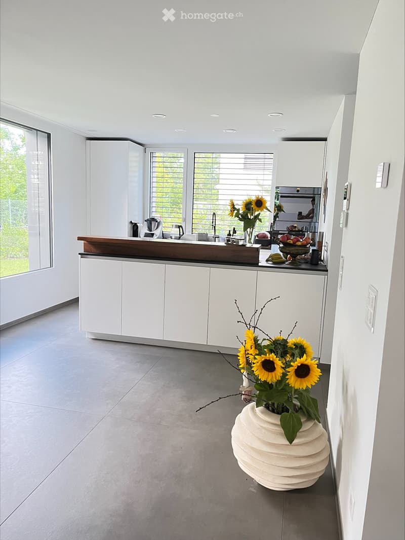 Modern kitchen with white cabinets, a wooden countertop, and a large vase with sunflowers on the floor.