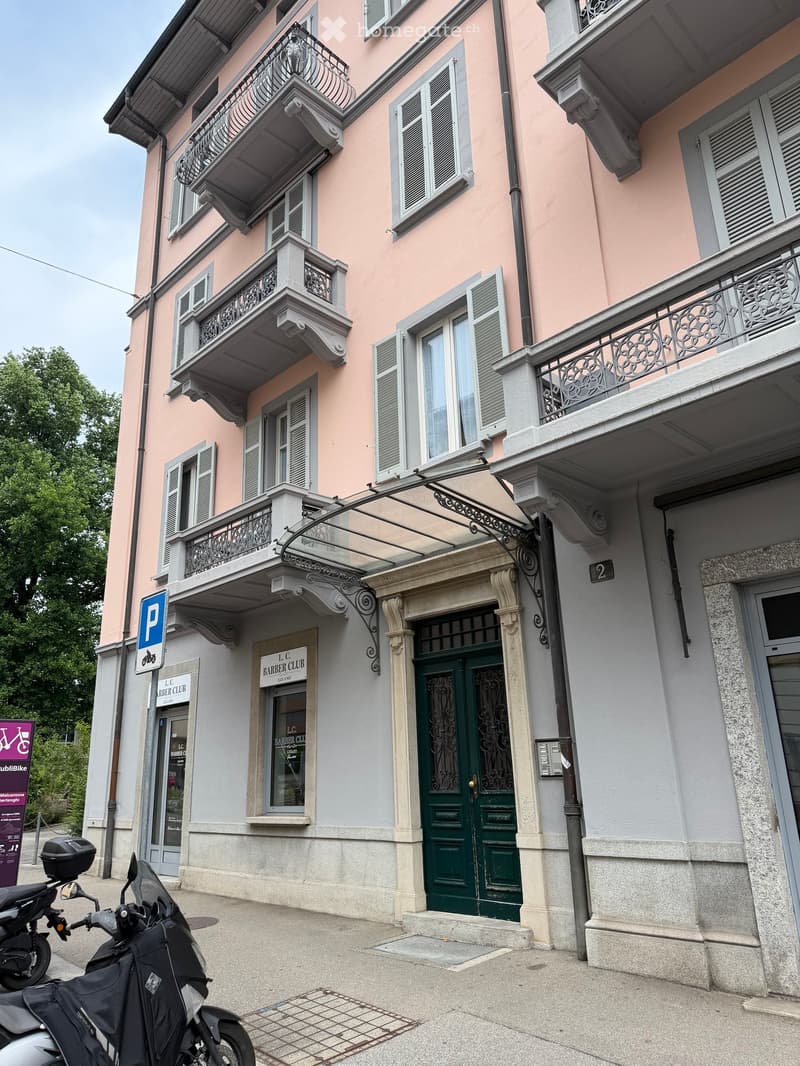 Multi-story building with pink facade, multiple balconies, ornate railings, green double doors, and a sign for "L.C. Barber Club".