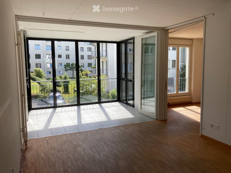 Empty room with wooden flooring, large sliding glass doors leading to a balcony, and natural light streaming in.