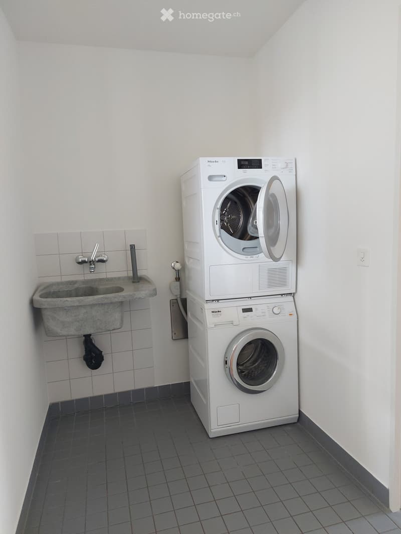 A small bathroom with a stacked washing machine and dryer, a sink with a faucet, and tiled walls and floor.