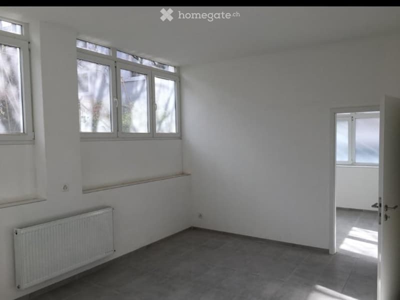 Empty room with white walls, tiled floor, radiator, and multiple windows allowing natural light.