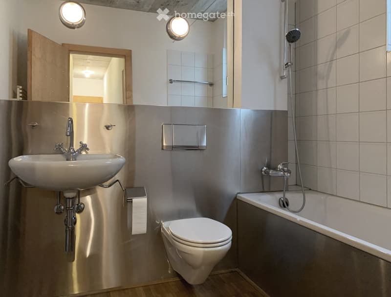 Modern bathroom with a sink, toilet, bathtub, and showerhead. Features a large mirror, light fixtures, and a wooden door leading to another room.