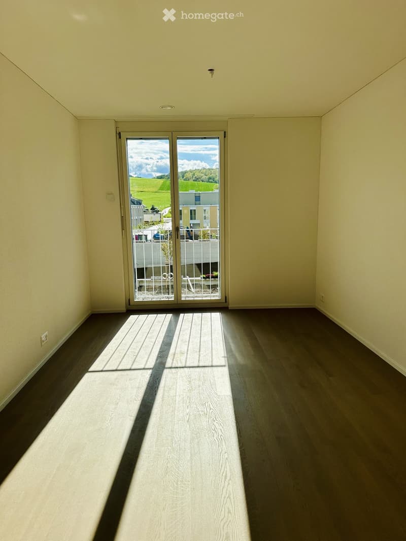 Empty room with wooden flooring and large sliding glass doors leading to a balcony with a view of a green landscape.