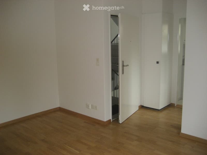 Empty hallway with wooden flooring, white walls, and a partially open door leading to another room.
