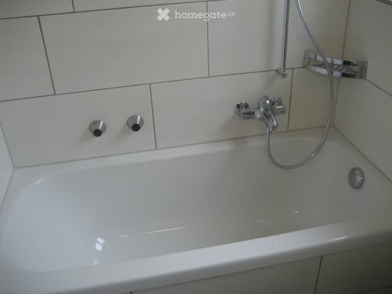 Bathtub with a modern faucet and handheld showerhead, surrounded by white tiled walls.