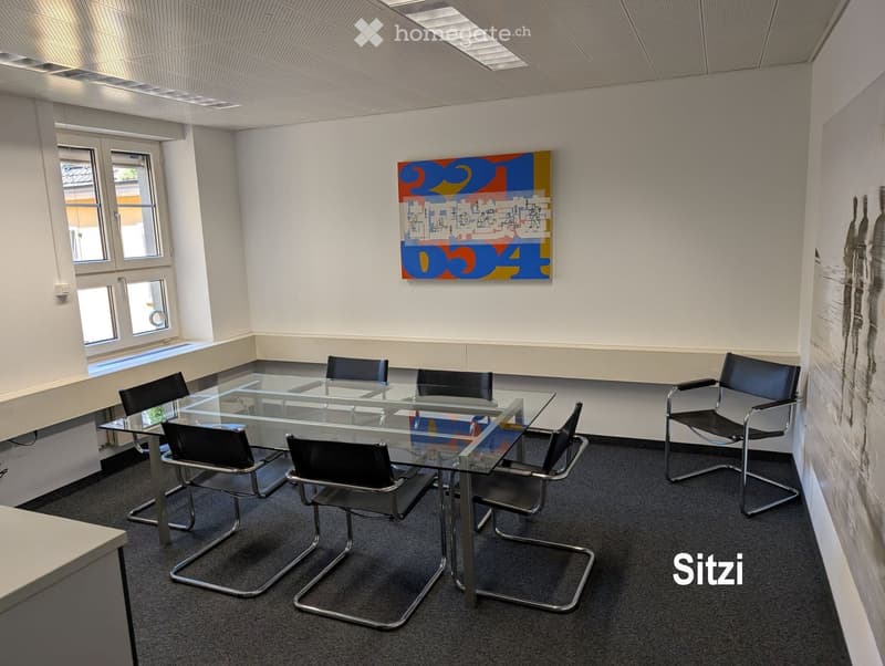Modern office space with a glass table surrounded by black chairs, large windows, and a colorful abstract painting on the wall.