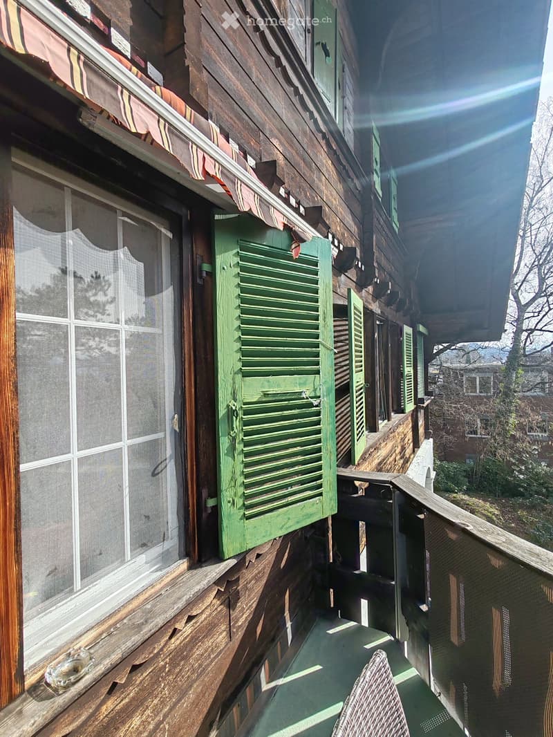 Balcony with wooden railings, green shutters, and a single wicker chair.
