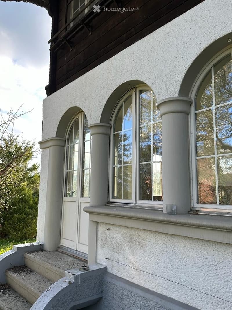 Exterior view of a two-story building with white stucco walls, arched windows, and decorative columns.