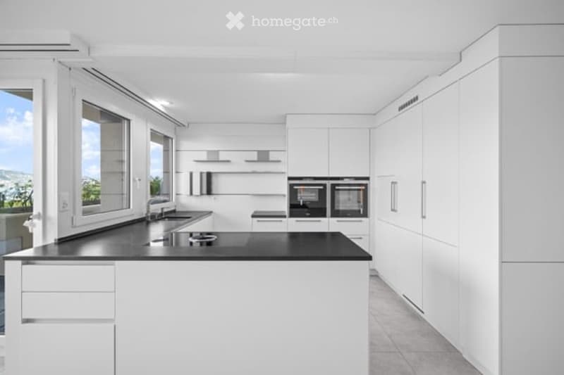 Modern, minimalist kitchen with white cabinets, black countertop, built-in oven, and large windows offering a scenic view.