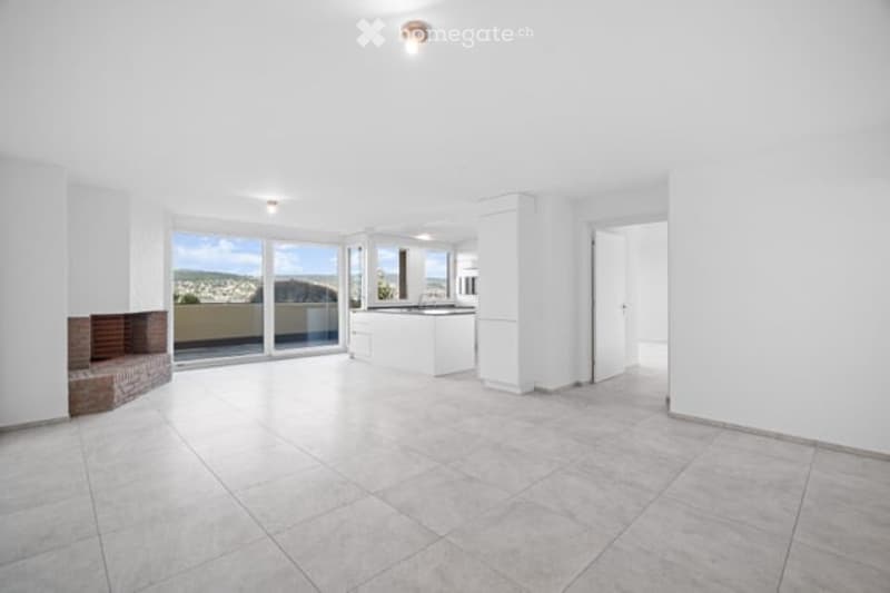 Bright, open-plan space with large glass doors leading to a balcony, tiled floor, white walls, and a view of the city and hills.