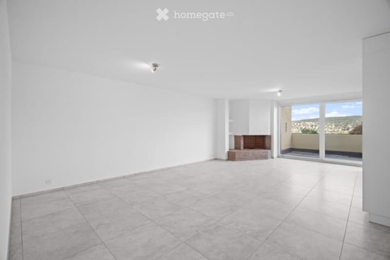 Empty room with white walls, tiled floor, fireplace, and large sliding glass doors leading to a balcony with a scenic view.